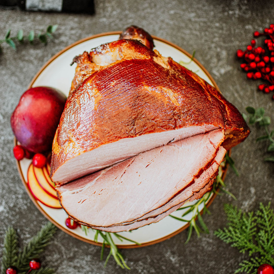 organic bone in half ham on a platter with apples, rosemary, and cranberries